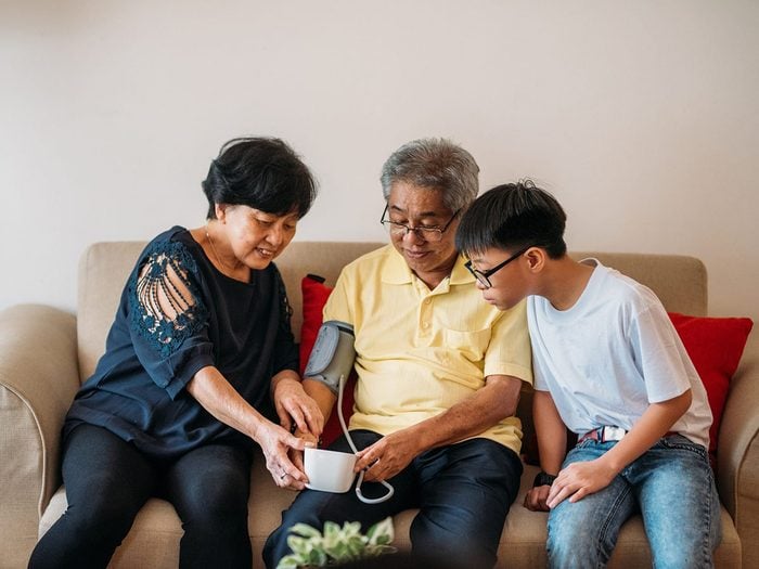 Image of Happy Asian Senior couple taking blood pressure with grandson in living room.