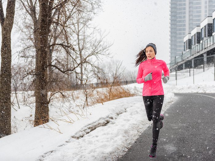 how your body deals with freezing weather - Winter running Asian girl wearing cold weather clothing for outside exercise in snow storm snowfall during winter training outdoors in city street. Fitness woman exercising.