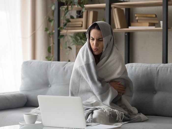Sick ill young woman feel cold covered with blanket sit on sofa watching movie on laptop, annoyed girl shiver freezing warming at home wrapped with plaid, no central heating problem and flu concept