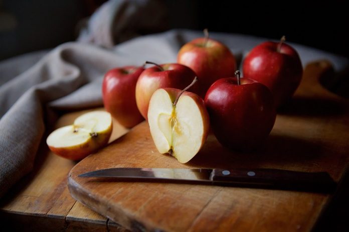 Яркие сочные красные яблоки лежат на старинном деревенском столе, вырезанном из половины яблока на переднем плане 2