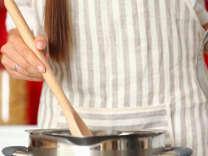 Woman cooking in kitchen stirring with wooden spoon