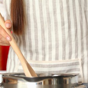 Woman cooking in kitchen stirring with wooden spoon