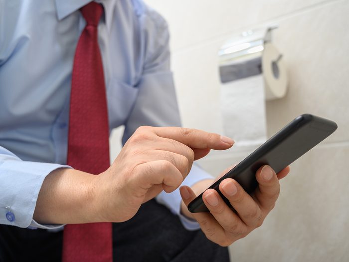 Germ spreading habits - man texting on toilet