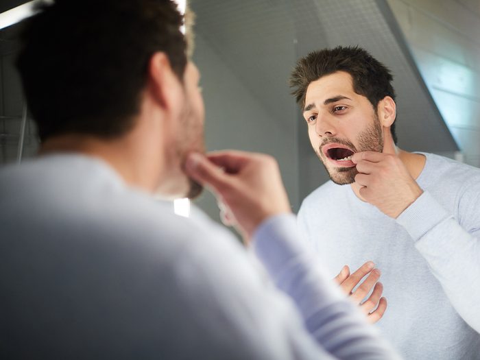 Oral cancer symptoms - man examining mouth in mirror