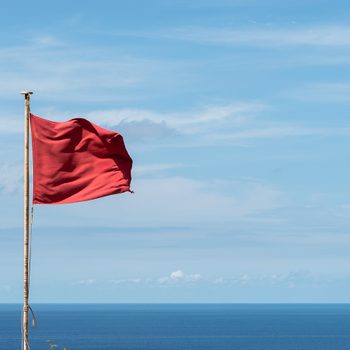Red flag waving on a pole. Clouds and sea view background. Horizontal View