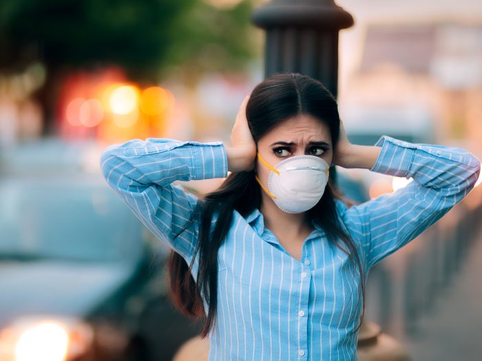 City noise is harmful to your health - woman in mask covering ears