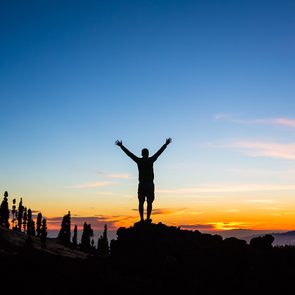 Man celebrating sunset with arms outstretched in mountains. Trail runner, hiker or climber with hands raised reached top of a mountain, inspirational landscape view on Tenerife, Canary Islands