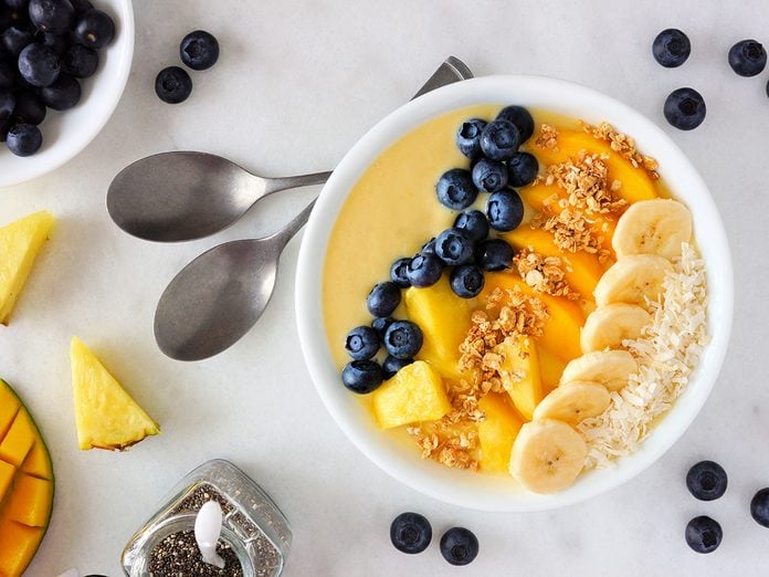 Healthy pineapple, mango smoothie bowl with coconut, bananas, blueberries and granola. Top view scene on a bright background.
