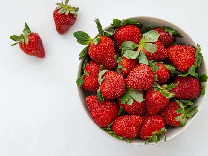 Ripe red strawberries on white bowl, over white background