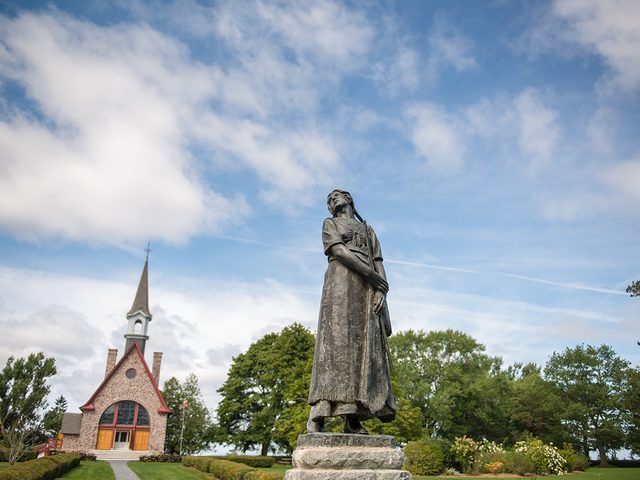 Historical places in every province - Evangeline Statue standing in the Victorian gardens with the Memorial Church in the background, Grand-Pre National Historic Site.