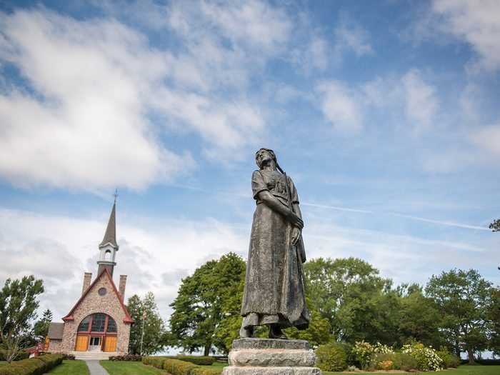 Historical places in every province - Evangeline Statue standing in the Victorian gardens with the Memorial Church in the background, Grand-Pré National Historic Site.
