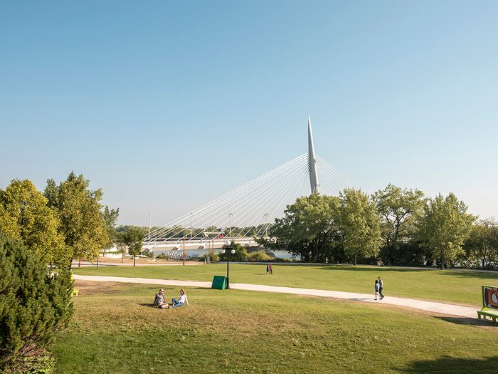 Historical places across Canada - Visitors enjoy the green space at Parks Canada Place. The Esplanade Riel pedestrian bridge is in the background. The Forks National Historic Site.