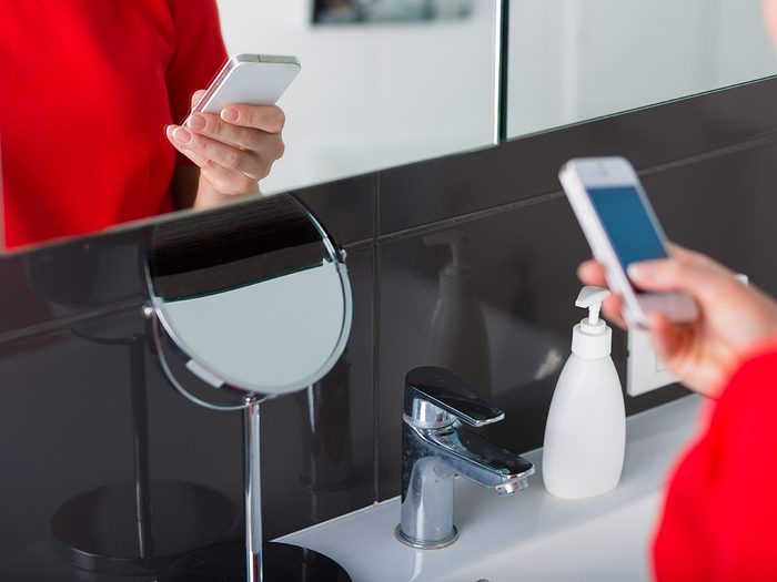 Woman standing by the mirror and holding a cell phone