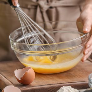 Female chef whisking eggs in glass bowl on kitchen table