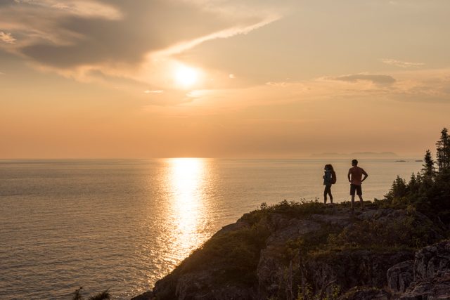 Best place to watch the sunset in every province - Visitors hiking the Manitou Miikna, "the spirit trail", at rocky outlook area at sunset. Pukaskwa National Park