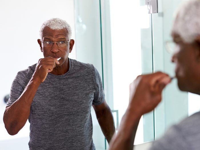 Mature man brushing teeth in mirror
