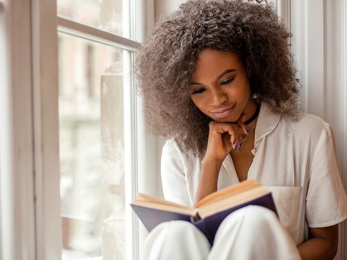Poet Sonnet L'Abbe - Pretty afro-american girl with reading a book sitting on the windowsill.