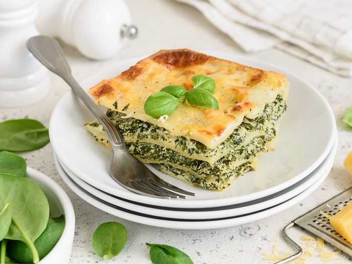A piece of lasagna with spinach, ricotta and bechamel sauce on a white plate. Traditional italian dish. Selective focus.