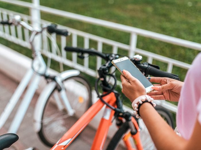 Bike theft prevention tips - In summer city background parking bicycles girl chooses route application, Internet online map phone. Route bike path. Bicycle parking city. Rental and blocking, protection application Internet.