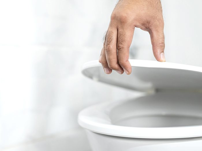 Cloudy urine - close up hand of a man closing the lid of a toilet seat. Hygiene and health care concept.