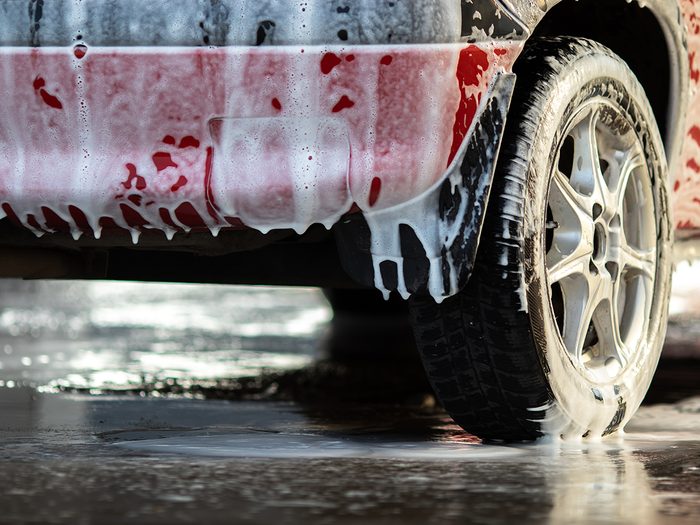 The back of a red passenger car at a car wash covered with foam. Close-up with a blurred background.