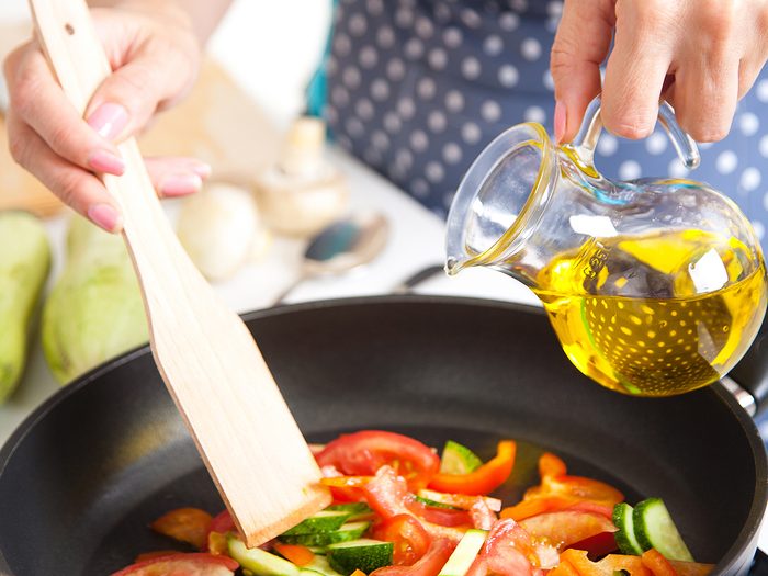 Healthiest cooking oil - woman adding oil to cooking veggies