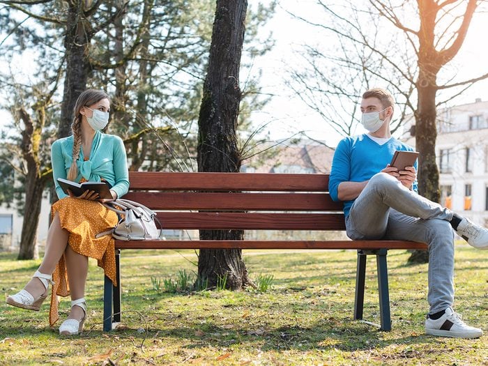 Woman and man in social distancing sitting on bench in park
