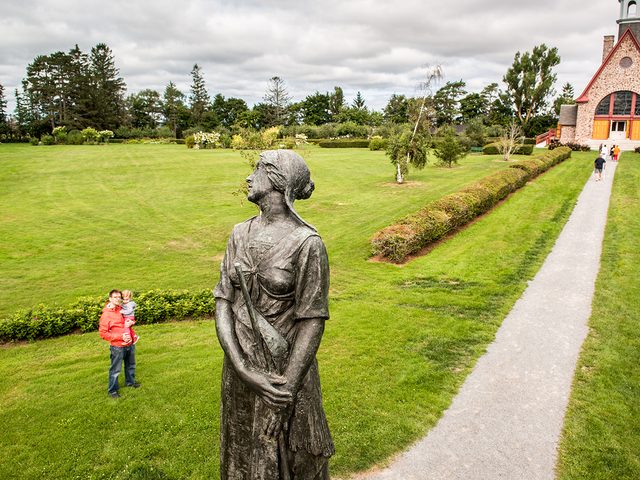 Visitors admiring the Statue of Evangeline in the Victorian Gardens with Memorial Church in background, Grand-Pre National Historic Site