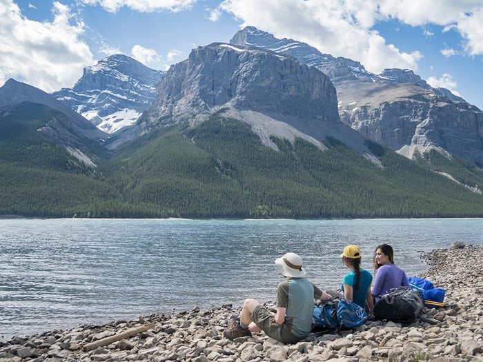 Two women and one man sitting by Lake Minnewanka at Aylmer Pass Junction backcountry campground. Banff National Park.