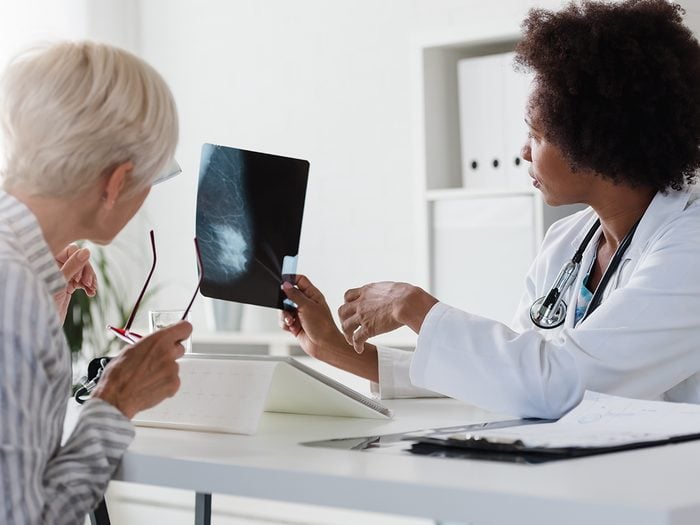 A female doctor sits at her desk and talks to a female patient while looking at her mammogram