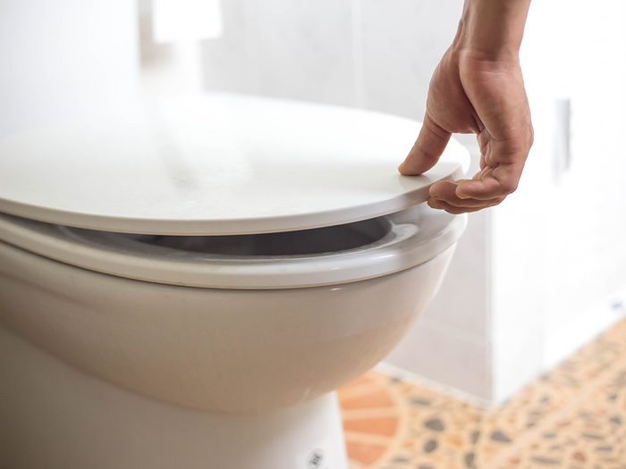 Why does poop float - hand of a man is closing the toilet lid. Prevents the spread of germs and viruses, Prevent air pollution, Concept of prevention of infection.