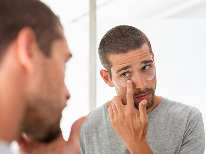 Man applying eye cream in mirror