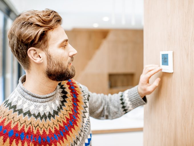 How to save money in Canada - young man adjusting thermostat