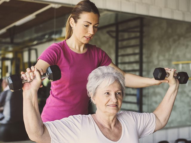 Senior woman lifting weights with personal trainer