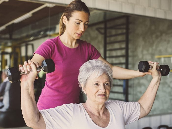 Senior woman lifting weights with personal trainer