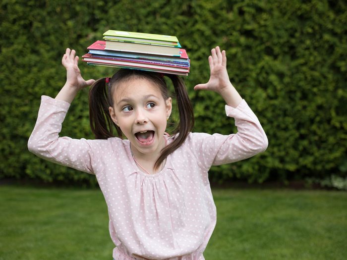 Little girl balancing stack of books on head