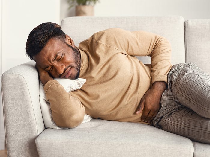 Signs of men's cancers - man with stomach pain on sofa