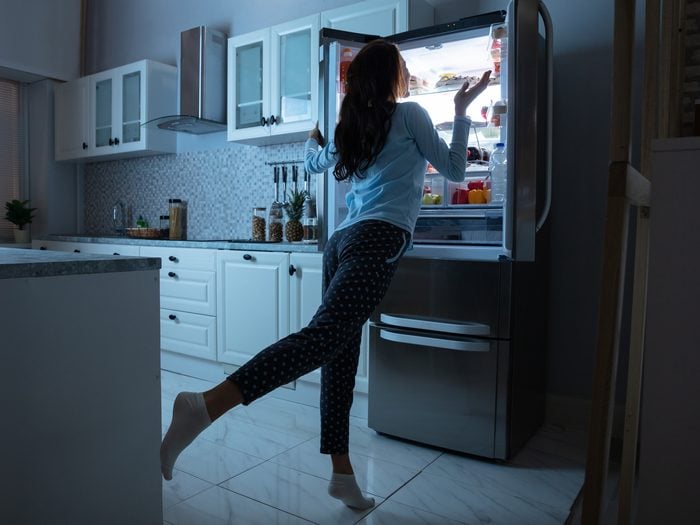 Food Before Bed - a woman looks inside the fridge at night