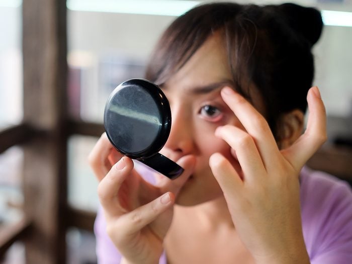 Woman examining eye in compact mirror