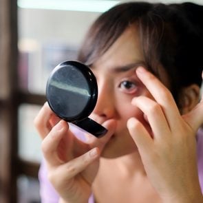 Woman examining eye in compact mirror