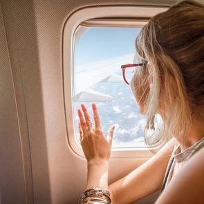 canada budget airline - Young woman enjoying the view through the aircraft window sitting during the flight in the airplane