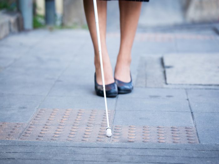 Blind woman is walking on the sidewalk using a cane
