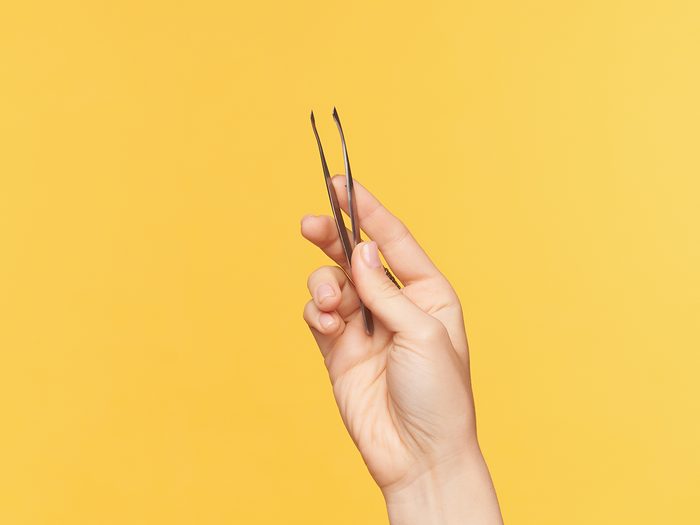 Hand holding tweezers against yellow backdrop
