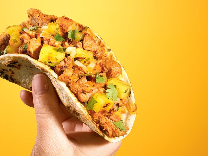 Hand holding a taco on yellow background