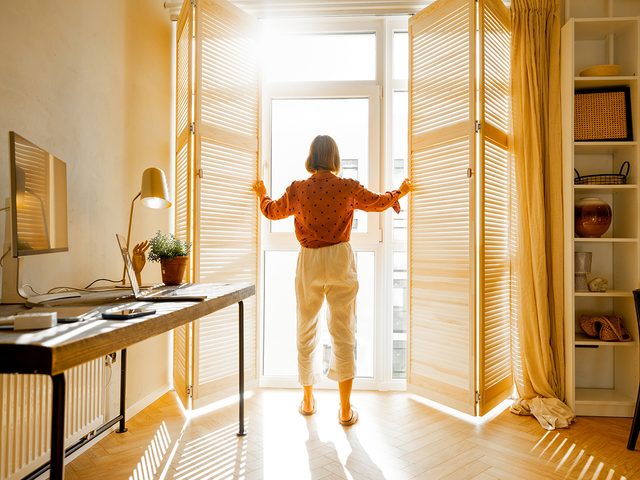 Woman opening shutters and letting sunshine in