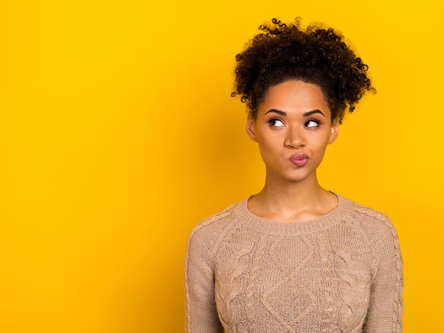 Woman with doubtful facial expression on yellow background