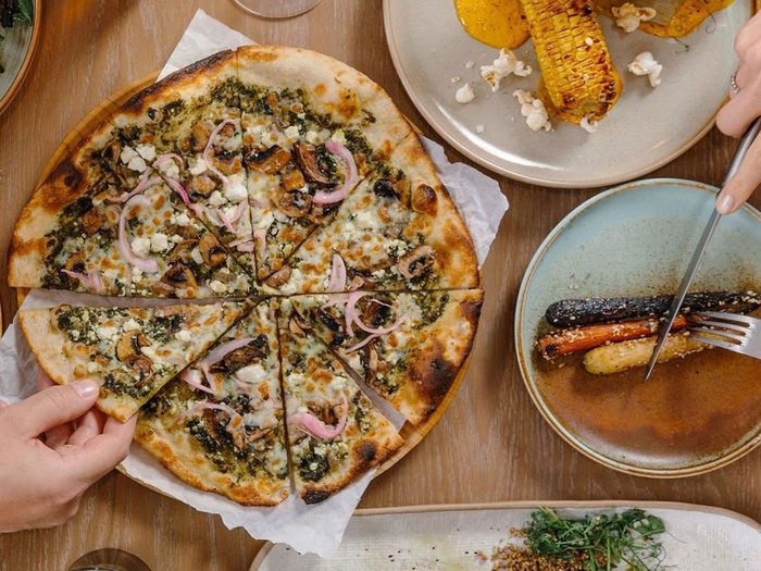 Best Restaurants In The Canadian Rockies - Farm And Fire - Pizza and person cutting food on plate