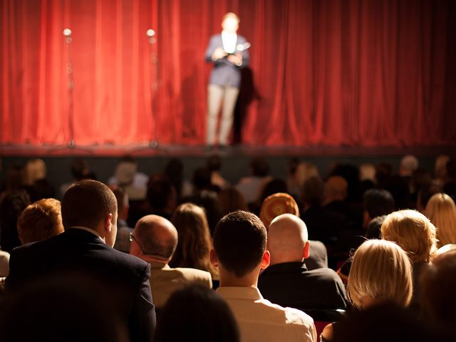 Yiddish Words - Schtick - Crowd watching person on stage with red curtain background